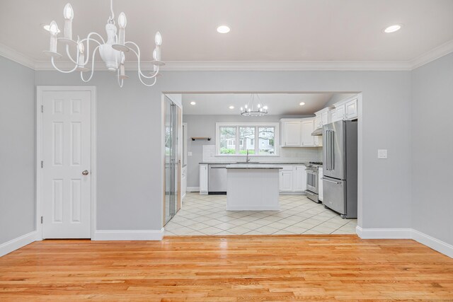 kitchen with high end appliances, light wood-style flooring, a sink, a notable chandelier, and white cabinetry