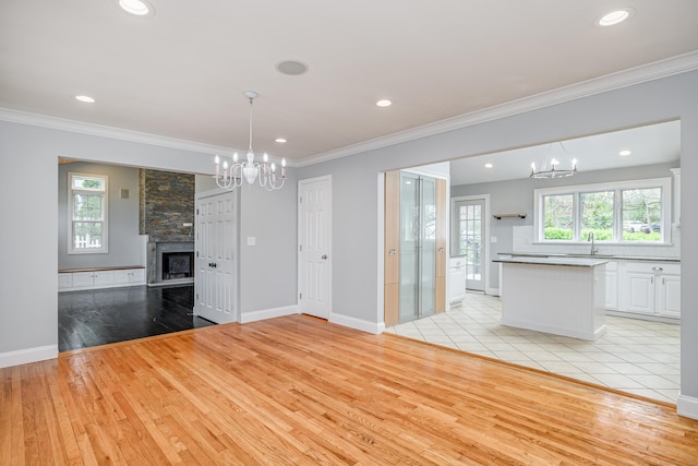unfurnished dining area with light wood-style floors, crown molding, a notable chandelier, and a large fireplace