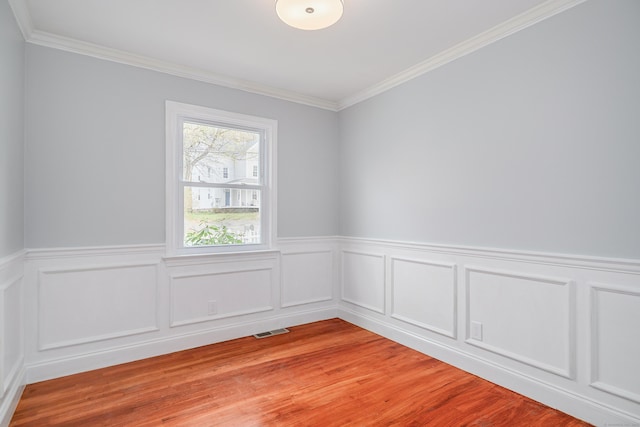 empty room with crown molding, wainscoting, light wood finished floors, and visible vents