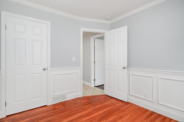 unfurnished bedroom featuring visible vents, ornamental molding, light wood finished floors, and a wainscoted wall