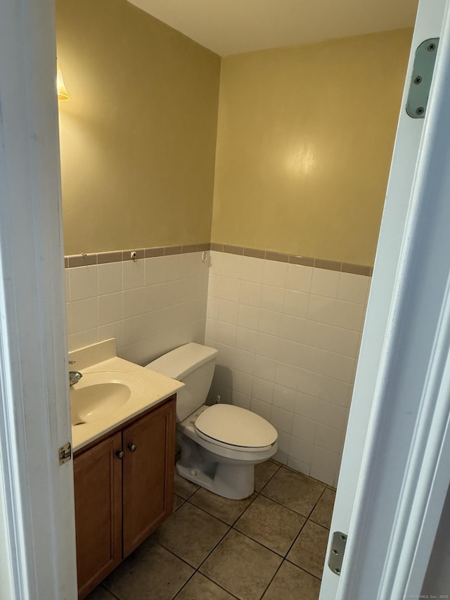 bathroom with a wainscoted wall, tile patterned floors, toilet, vanity, and tile walls