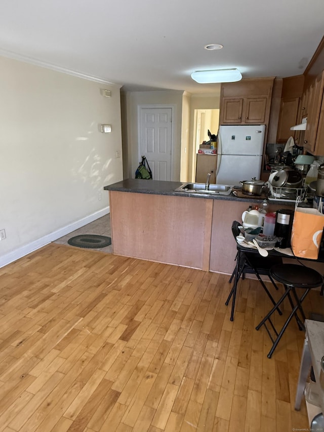 kitchen with light wood finished floors, a peninsula, dark countertops, freestanding refrigerator, and under cabinet range hood