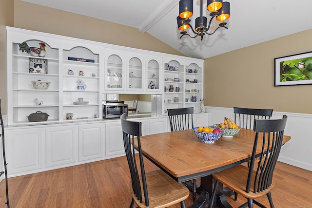 dining area featuring wainscoting, vaulted ceiling with beams, light wood-style floors, and a chandelier