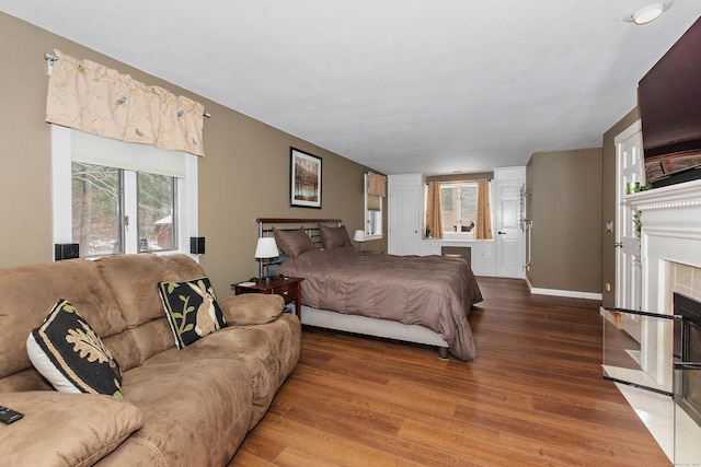 bedroom featuring baseboards, multiple windows, wood finished floors, and a fireplace
