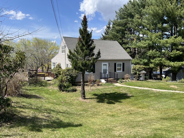view of front of home featuring a wooden deck, a shingled roof, and a front yard