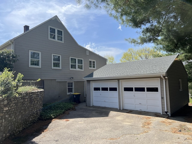 view of front of house featuring a chimney, driveway, a shingled roof, an outdoor structure, and a garage