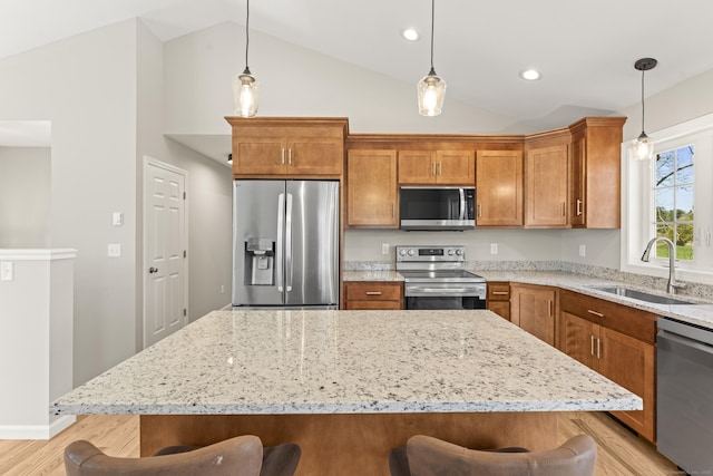 kitchen featuring brown cabinets, a breakfast bar, a sink, light stone countertops, and appliances with stainless steel finishes