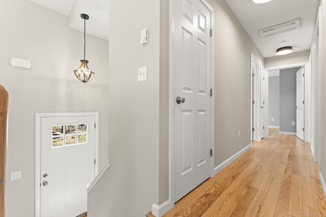 hallway with baseboards, visible vents, light wood finished floors, and an inviting chandelier