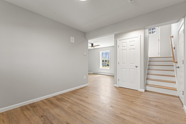 unfurnished room with baseboards, light wood-style flooring, baseboard heating, and stairway