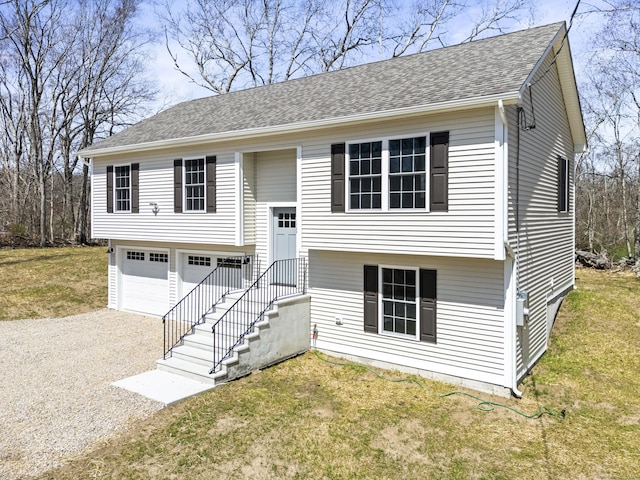 bi-level home featuring gravel driveway, roof with shingles, a garage, and a front yard