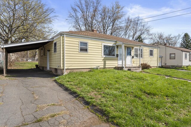 view of front of home with a carport, driveway, a chimney, and a front lawn