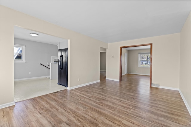 unfurnished living room featuring a healthy amount of sunlight, light wood finished floors, baseboards, and visible vents
