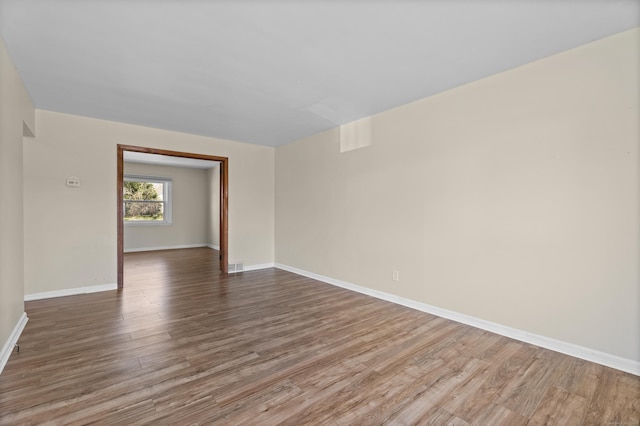 empty room featuring wood finished floors, visible vents, and baseboards