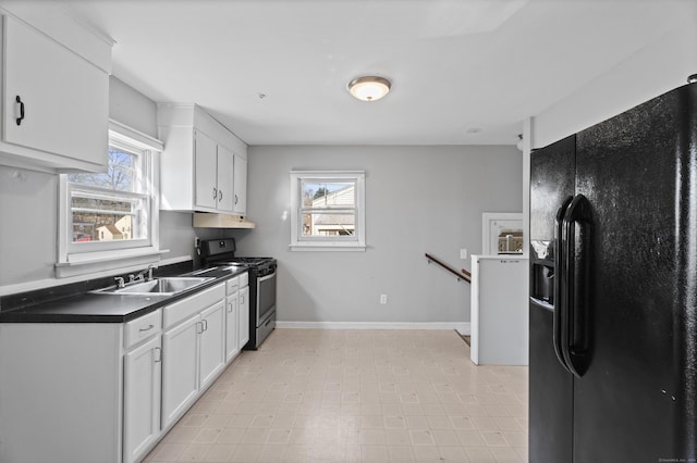 kitchen featuring white cabinets, a sink, stainless steel gas range, black fridge, and dark countertops