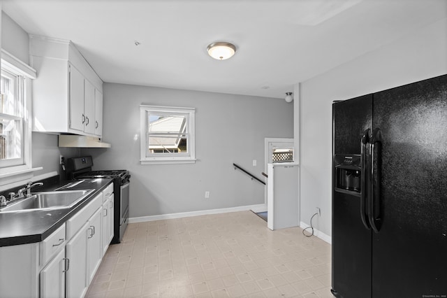 kitchen featuring stainless steel gas range oven, dark countertops, a sink, black fridge with ice dispenser, and white cabinetry