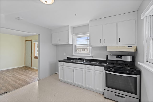 kitchen featuring white cabinets, a sink, dark countertops, under cabinet range hood, and stainless steel gas range oven