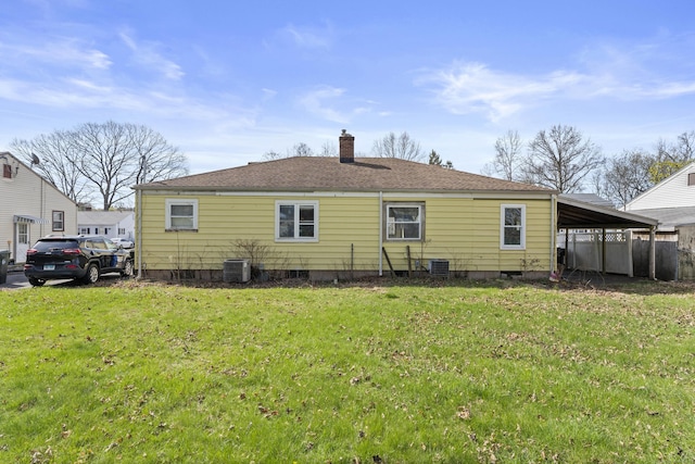 rear view of house with a chimney, an attached carport, roof with shingles, and a lawn