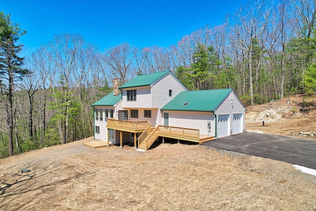 view of front of home with a chimney, stairway, metal roof, a wooden deck, and a forest view