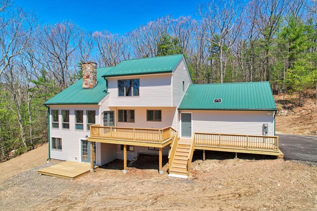 rear view of house with a deck, a chimney, driveway, and metal roof