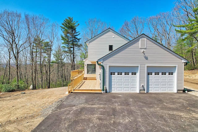 view of side of home with a wooden deck, an attached garage, and aphalt driveway