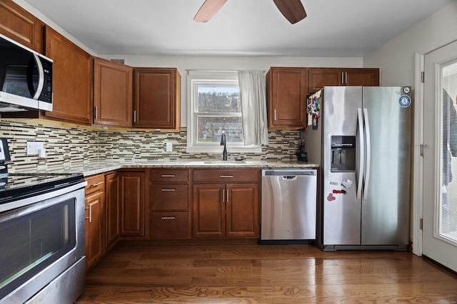kitchen with appliances with stainless steel finishes, tasteful backsplash, a sink, and dark wood-type flooring