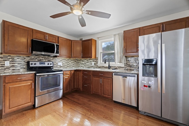 kitchen featuring a sink, decorative backsplash, light wood-style floors, ceiling fan, and appliances with stainless steel finishes