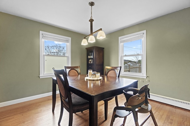 dining room featuring a baseboard heating unit, baseboards, and light wood-type flooring