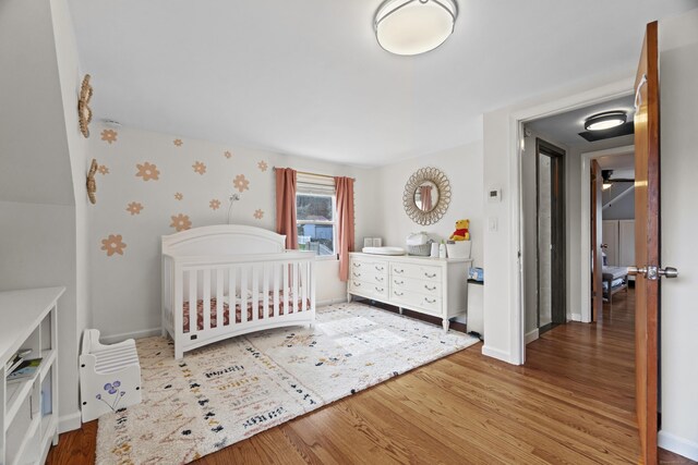 bedroom featuring baseboards, wood finished floors, a nursery area, and wallpapered walls