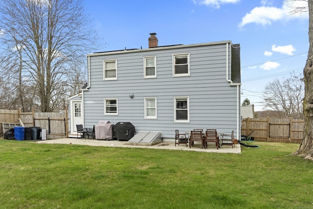 rear view of property with a yard, a patio area, a fenced backyard, and a chimney