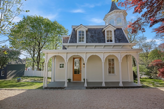 view of front of property with fence, a front yard, roof with shingles, mansard roof, and a porch