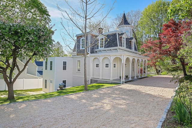 view of front of home featuring fence, a porch, a chimney, mansard roof, and driveway