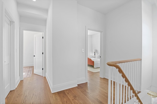 hallway featuring baseboards, recessed lighting, wood finished floors, and an upstairs landing