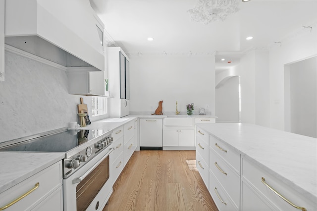 kitchen featuring arched walkways, high end white range, a sink, white cabinets, and light wood-style floors