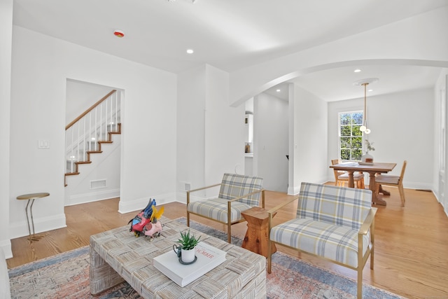 living area featuring stairs, arched walkways, recessed lighting, and light wood-style floors