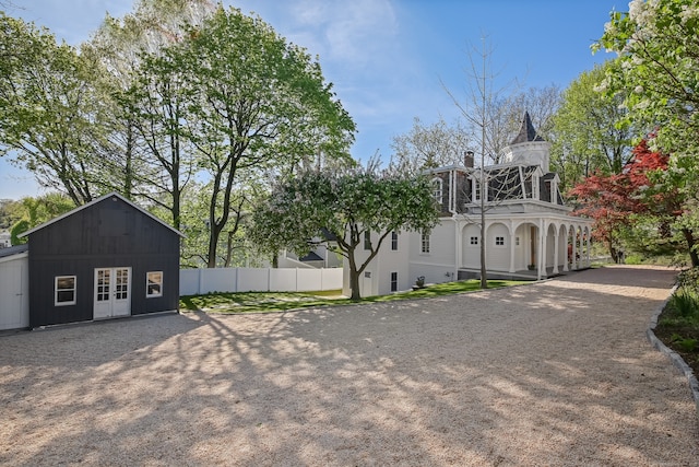 view of front of house featuring driveway, french doors, a chimney, mansard roof, and fence
