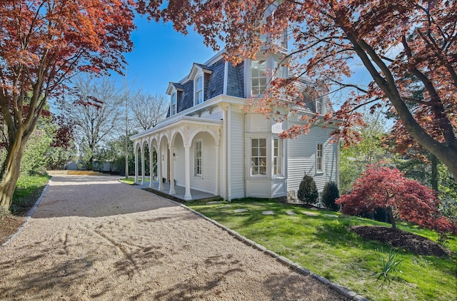 view of property exterior featuring a porch, a lawn, mansard roof, and driveway