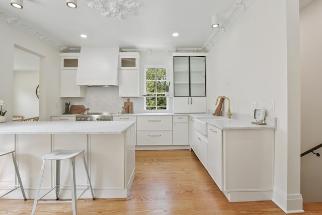 66 Seminary St, New Canaan, CT 06840 - kitchen with premium range hood, a kitchen bar, glass insert cabinets, white cabinetry, and light wood finished floors