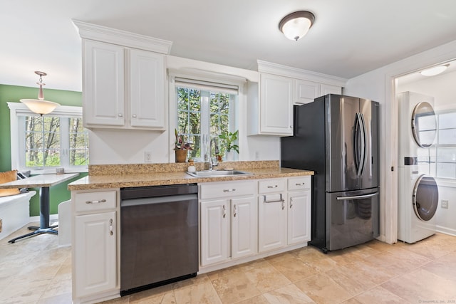 kitchen with stainless steel appliances, stacked washer / drying machine, white cabinetry, and a sink