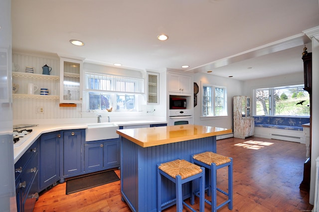 kitchen featuring a breakfast bar area, light wood-style floors, baseboard heating, blue cabinetry, and white appliances