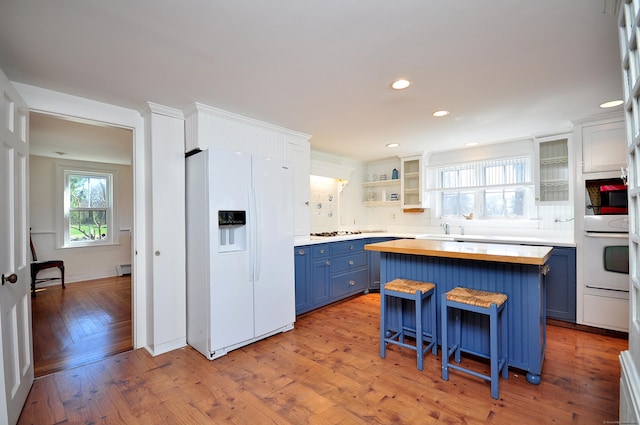 kitchen featuring white appliances, blue cabinetry, butcher block countertops, a sink, and a center island