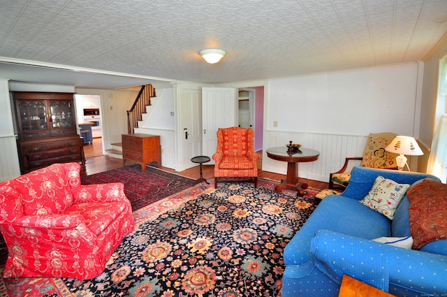 living room featuring crown molding, a wainscoted wall, stairs, and wood finished floors