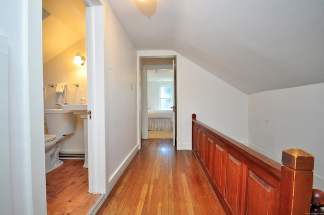 corridor with lofted ceiling, light wood-style floors, an upstairs landing, and baseboards