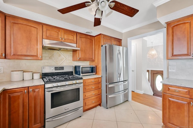 kitchen with brown cabinetry, crown molding, under cabinet range hood, appliances with stainless steel finishes, and light tile patterned floors