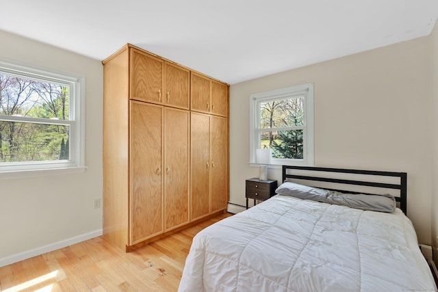 bedroom with a closet, baseboards, a baseboard heating unit, and light wood-type flooring