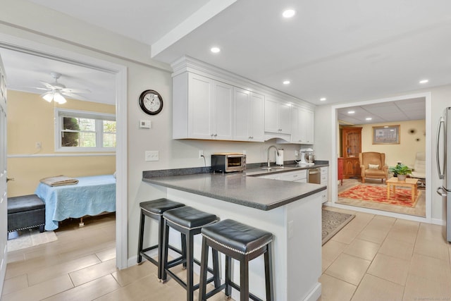 kitchen with white cabinets, dark countertops, a sink, a breakfast bar area, and stainless steel appliances