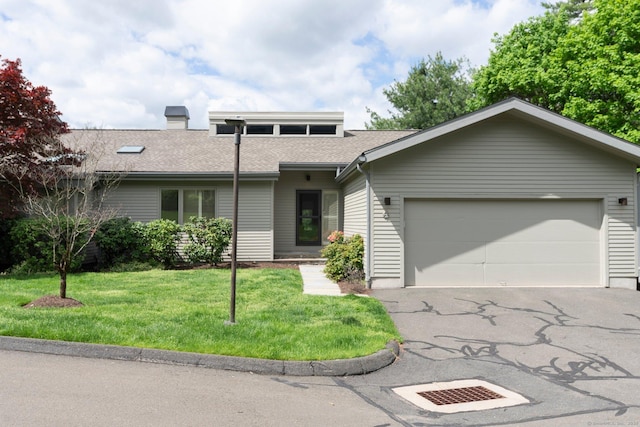 view of front of property with an attached garage, asphalt driveway, a front yard, a chimney, and a shingled roof