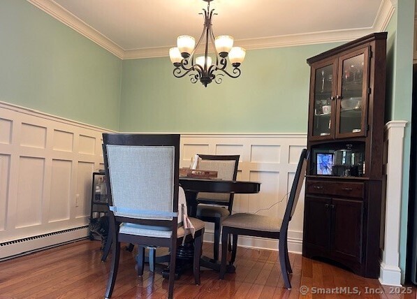dining space with crown molding, a baseboard radiator, a decorative wall, and a chandelier