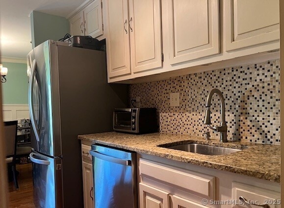 kitchen featuring decorative backsplash, white cabinets, light stone counters, a sink, and dishwasher