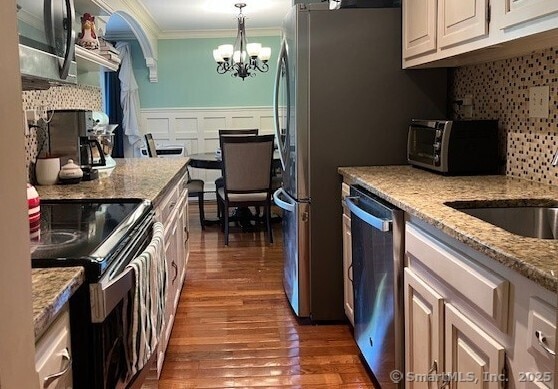 kitchen with crown molding, tasteful backsplash, wood finished floors, an inviting chandelier, and stainless steel appliances