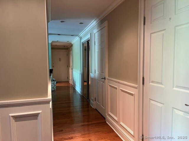 corridor featuring wood finished floors, wainscoting, crown molding, and a decorative wall